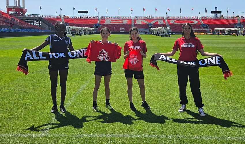 Four women in soccer field holding banners