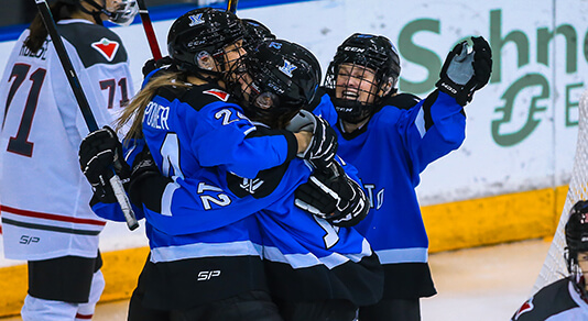 Women hockey players celebrating in a group hug