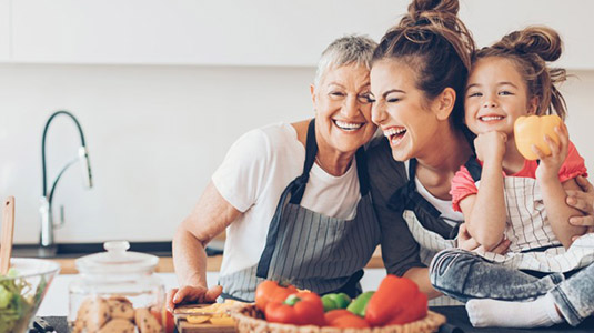 Grandmother, mother and young daughter at kitchen counter happily preparing a meal