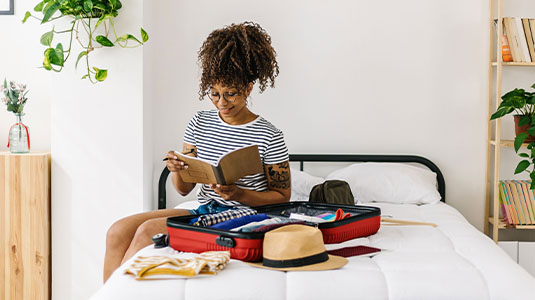 Young woman writing in a book sitting alongside her packed luggage
