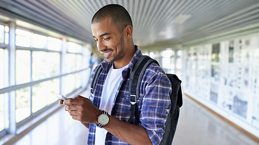 Man in a hallway looking at a phone smiling.