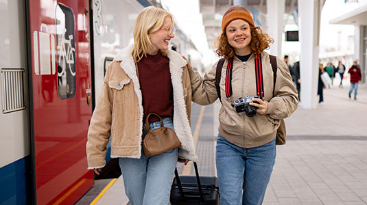 Two young adults walking with luggage, laughing.