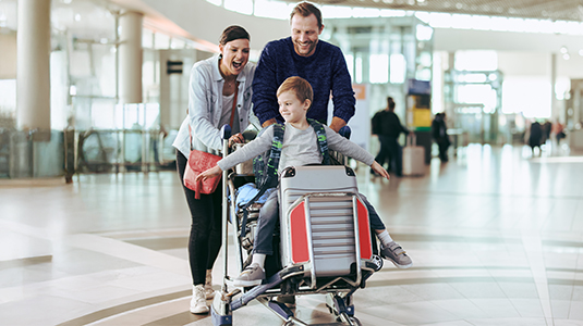 Parents pushing luggage with a kid through airport laughing.
