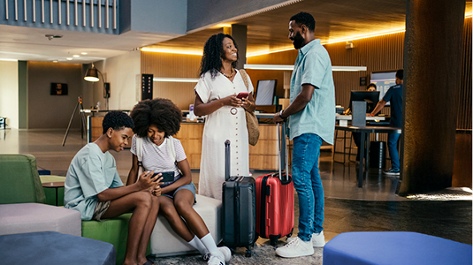 Family sitting in a hotel lobby with their luggage talking.