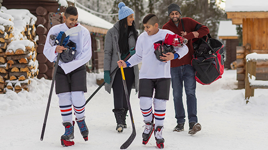 A couple at an outdoor rink watch their two kids playing hockey