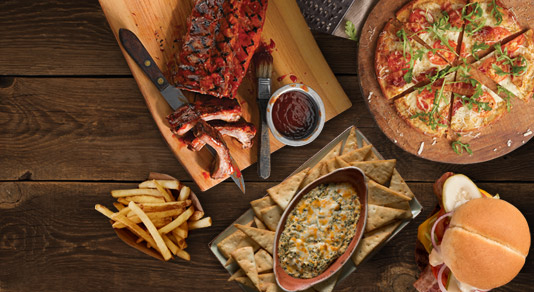 pizza, burger, ribs, fries, and spinach dip on wooden board
