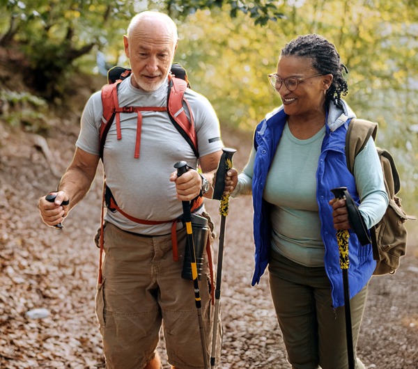 An older couple hiking in the woods with full gear.