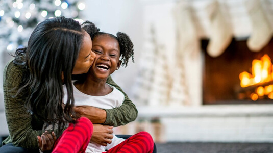 Mother and daughter cuddling in front of a holiday fireplace