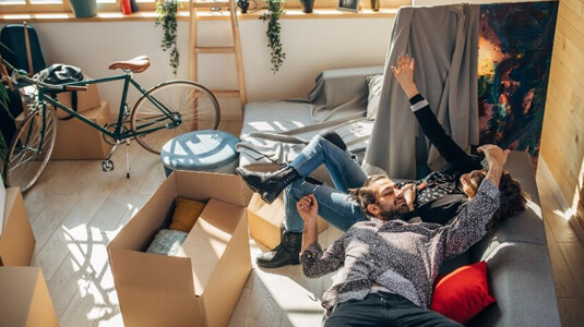 Young couple relaxing on a couch surrounded by unpacked boxes in an apartment living room