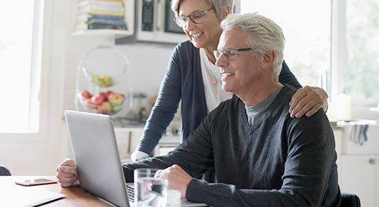 An elderly couple staring at the computer, planning a trip.