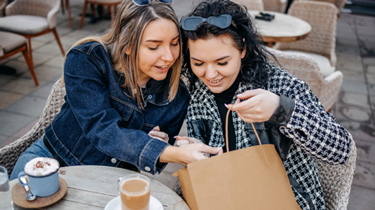 Two friends looking at their purchases inside a shopping bag