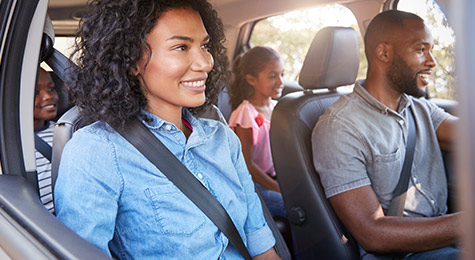 A happy family in a car wearing seat belts.
