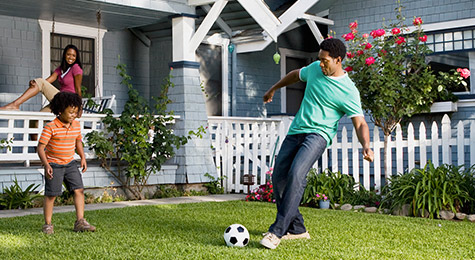 Two kids playing soccer in front yard.