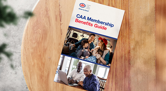 CAA Membership benefits guide digital on a wood table.