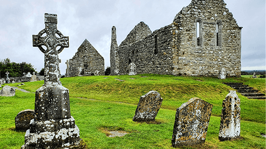 Weathered stone church ruins with stone Celtic cross.