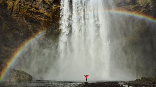 Skógafoss waterfall with rainbow and solo traveller.