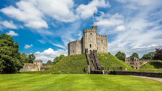 Castle on top of a green hill with long stairs and path leading up to it.