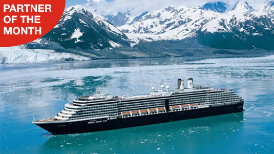 Holland America Line cruise ship one water with mountains covered in snow in background. Partner of the month.