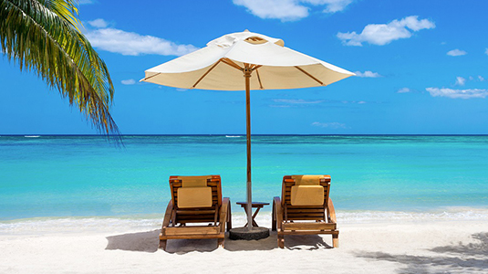 Two beach chairs and an umbrella set up on the beach looking at the ocean