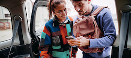 A couple standing at an open car back door looking at a phone