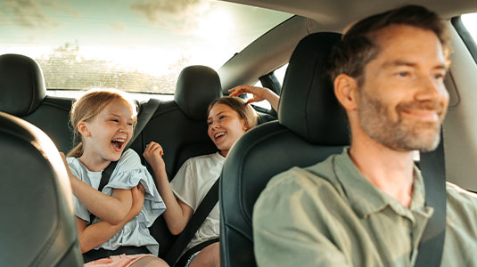A father driving a car with his two daughters in the backseat