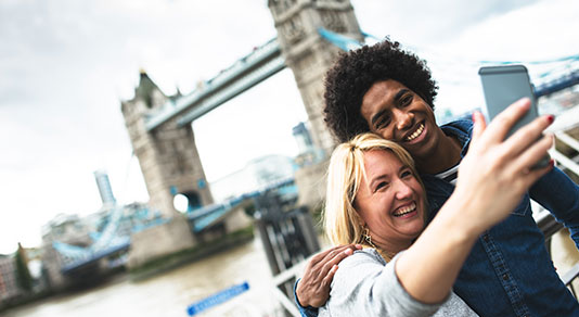 Ethnic travelers taking a selfie with London Bridge in background.