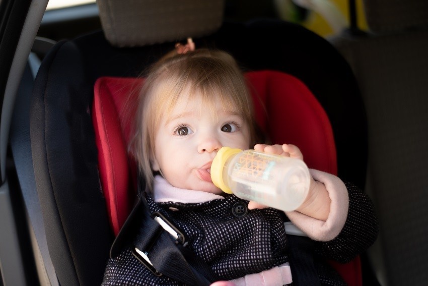 Baby girl is drinking from a water bottle while in car strapped in her booster seat