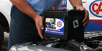 A CAA representative holding a CAA battery on hood of car